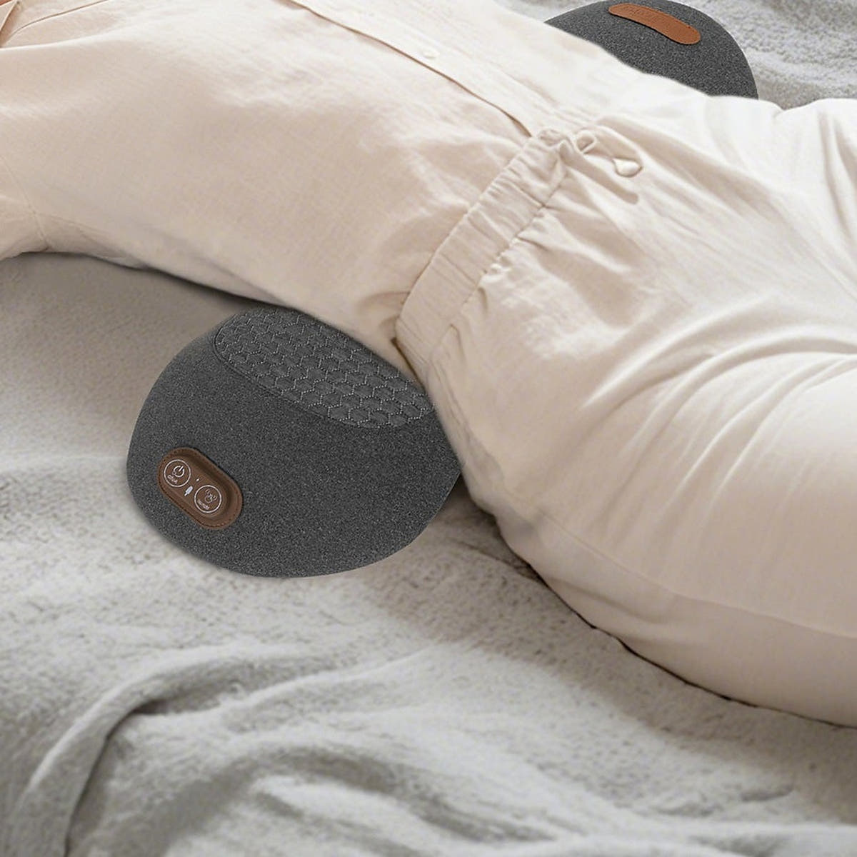 Back massager pillow with heat placed under the lower back of a person lying on a bed