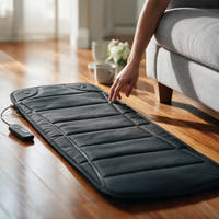 Full body massage mat in use, unrolled on hardwood floor beside a sofa